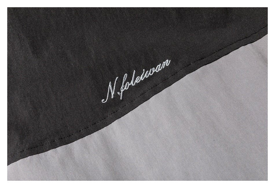 White cursive embroidery on the black panel of a gray and black garment.