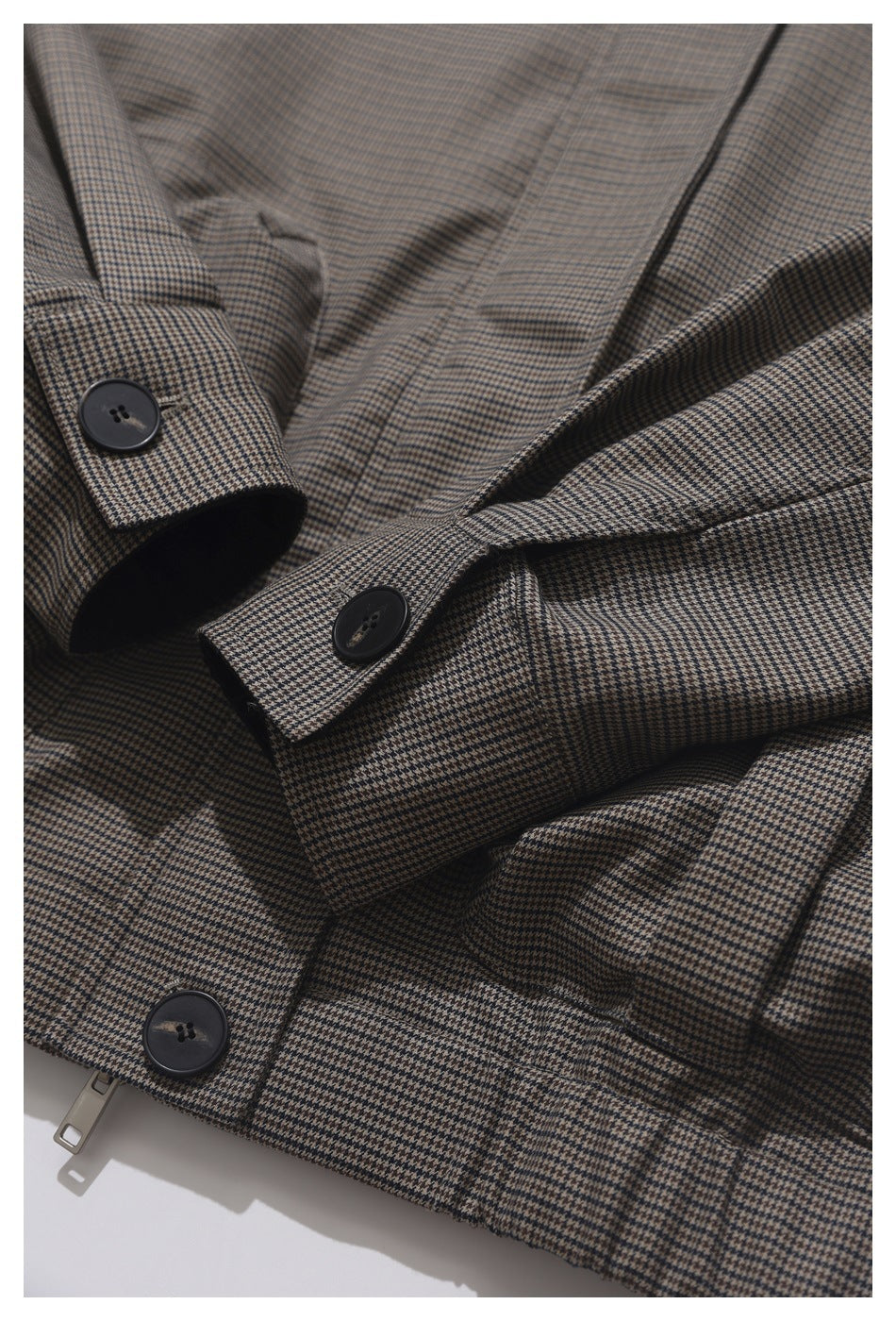 Close-up of a brown and black houndstooth jacket showing dark buttons, a zipper, and folded fabric.