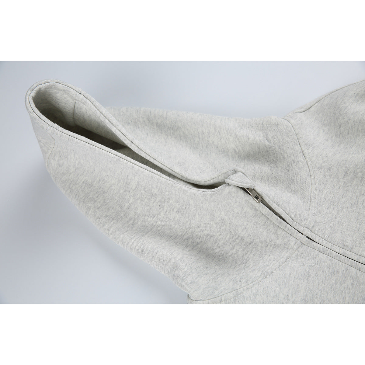 Close-up of a light gray hoodie’s hood opening and zipper pull.