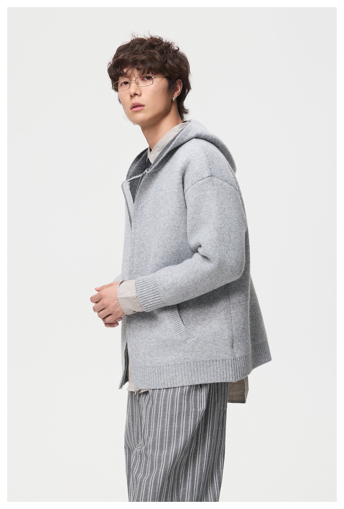 Side view of a model wearing a light gray hooded knit jacket with a front zipper and ribbed trim.