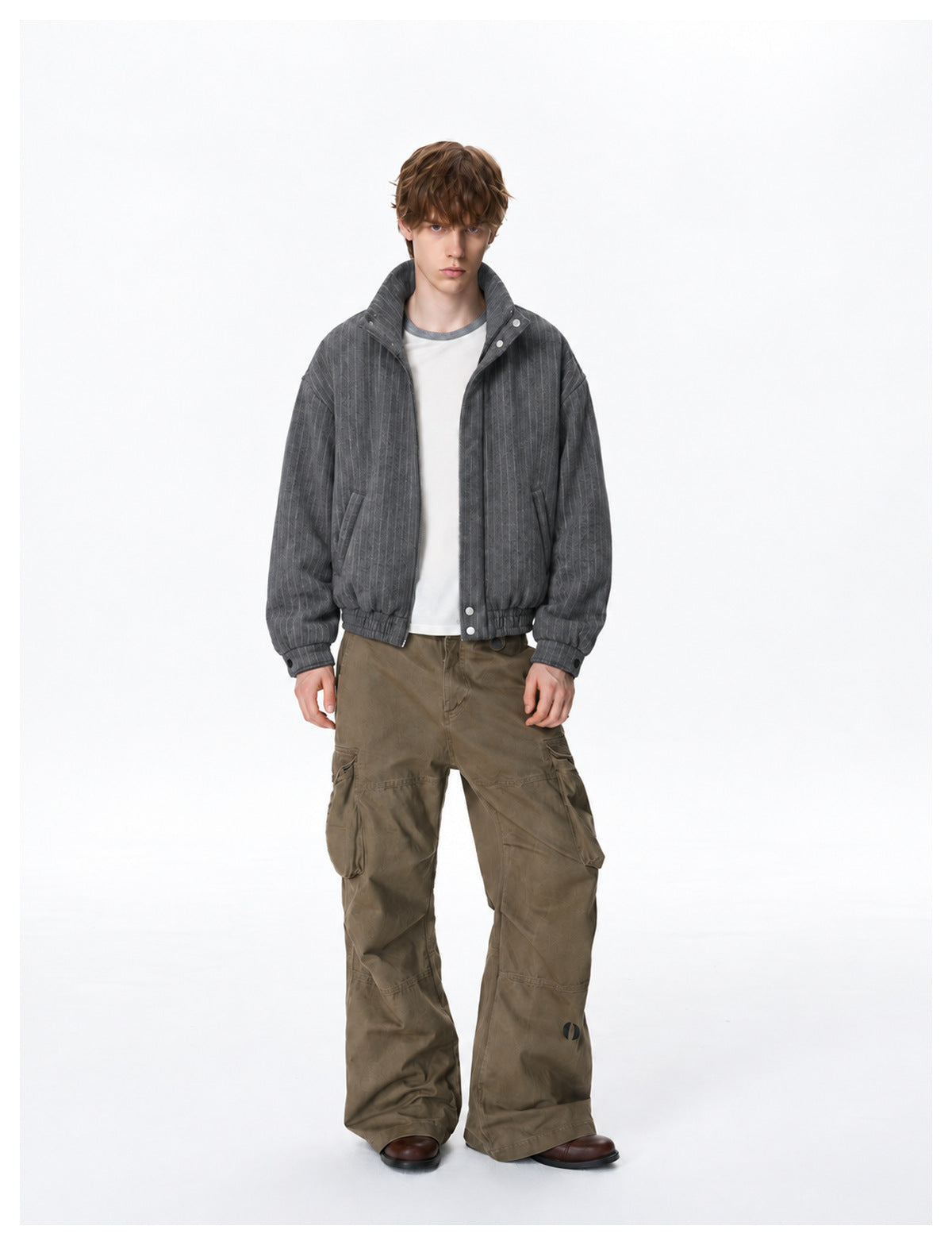 Full-length view of a model in a dark gray pinstriped bomber jacket, white tee and wide-leg brown cargo pants