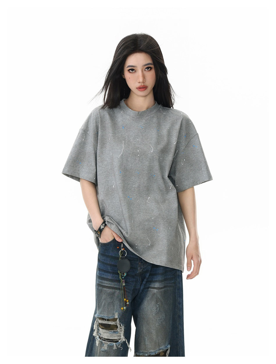 Front view of a model in an oversized gray short-sleeve T-shirt with scattered blue and white marks and distressed jeans.