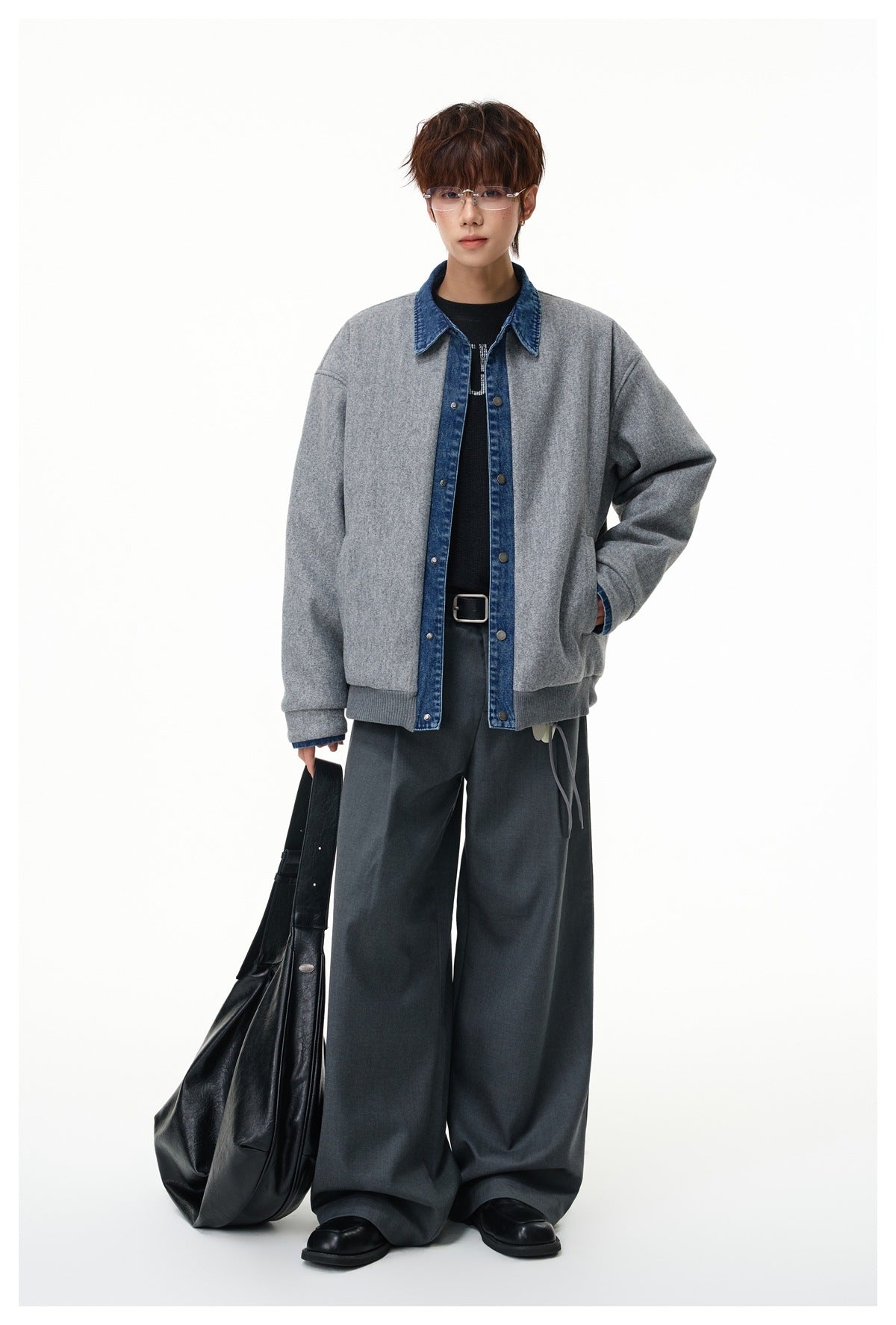 Full-length model wearing a light gray jacket with blue denim trim and wide-leg trousers, holding a large black bag.