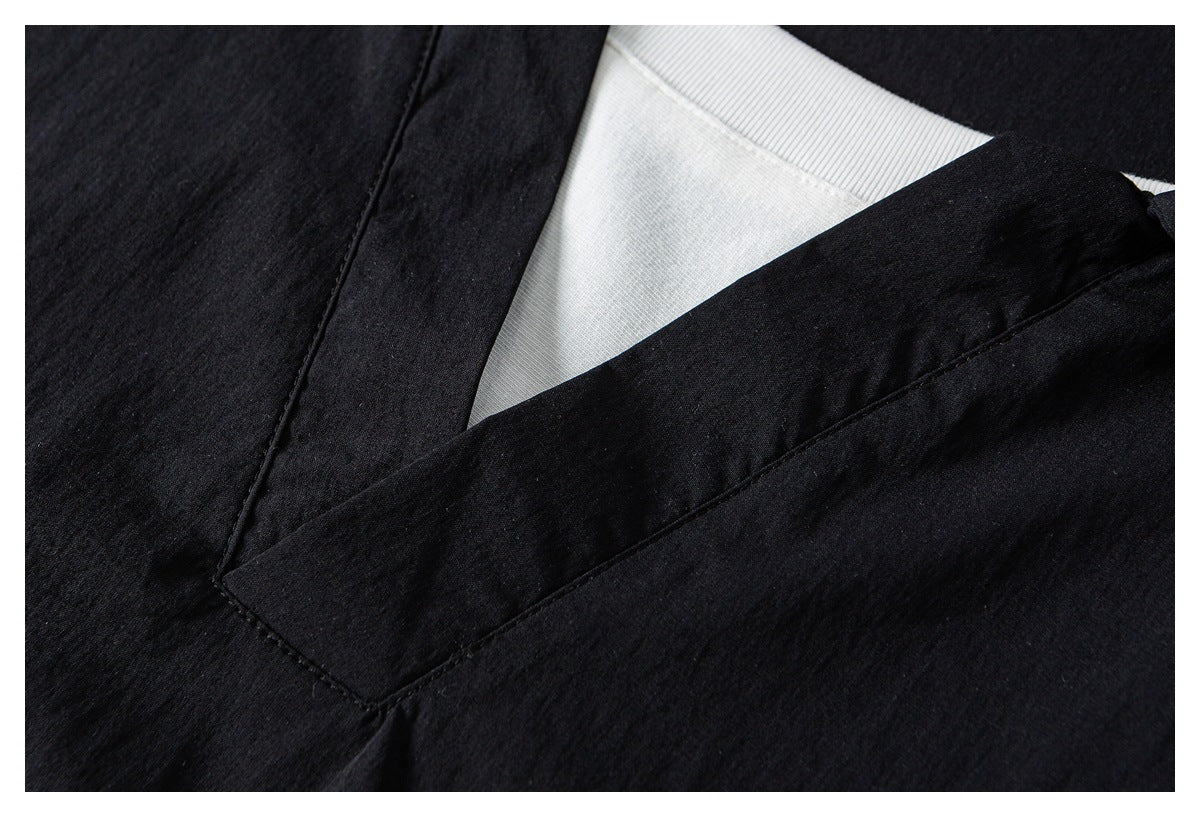 Close-up of a black garment's V-neck opening and stitched front band, with a white inner layer visible.