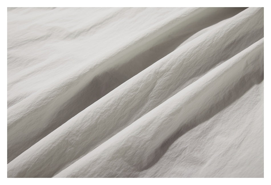 Macro view of pale gray garment fabric draped into folds, showing its lightly crinkled surface.