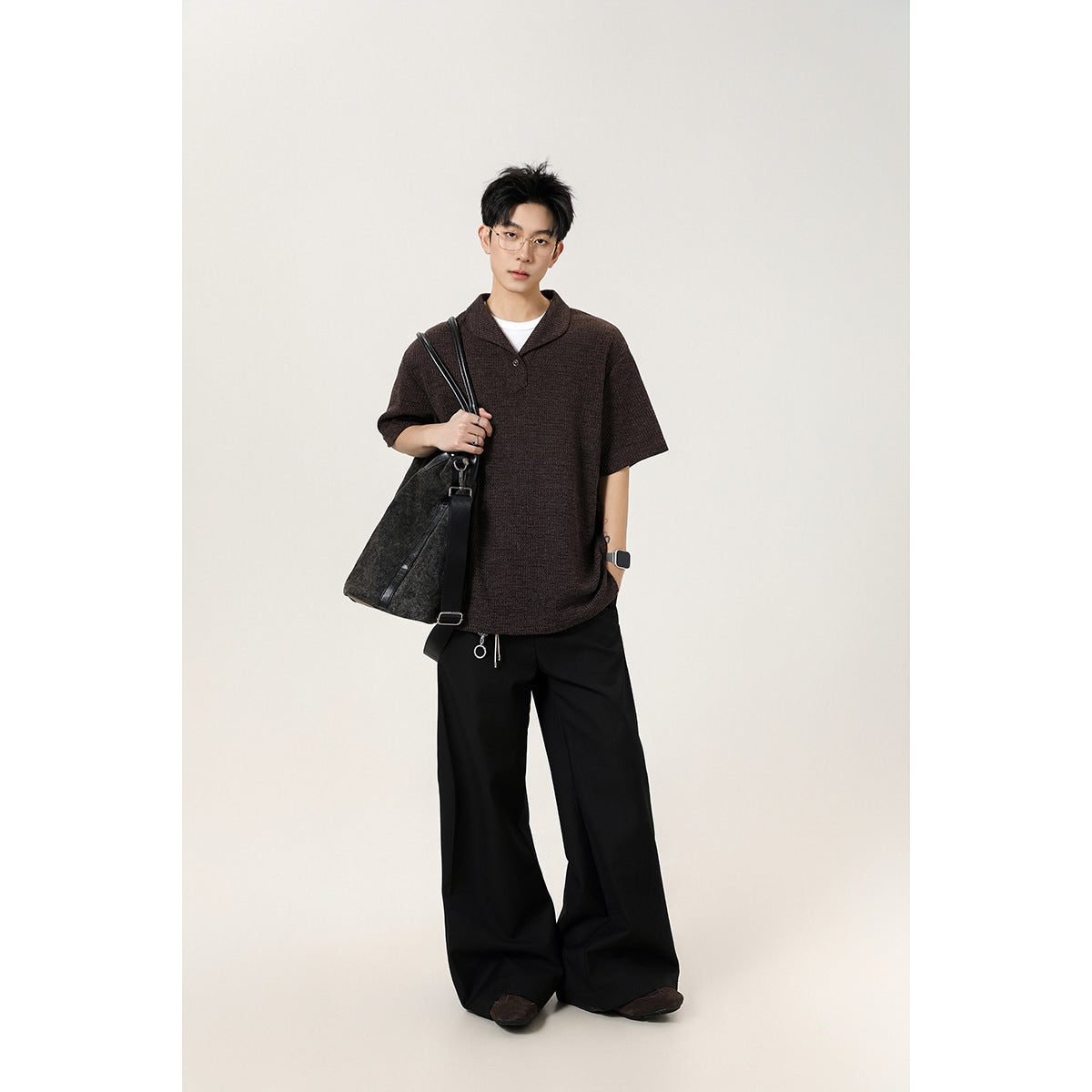 Full-length model wearing a dark brown short-sleeve knit polo shirt and loose black trousers.