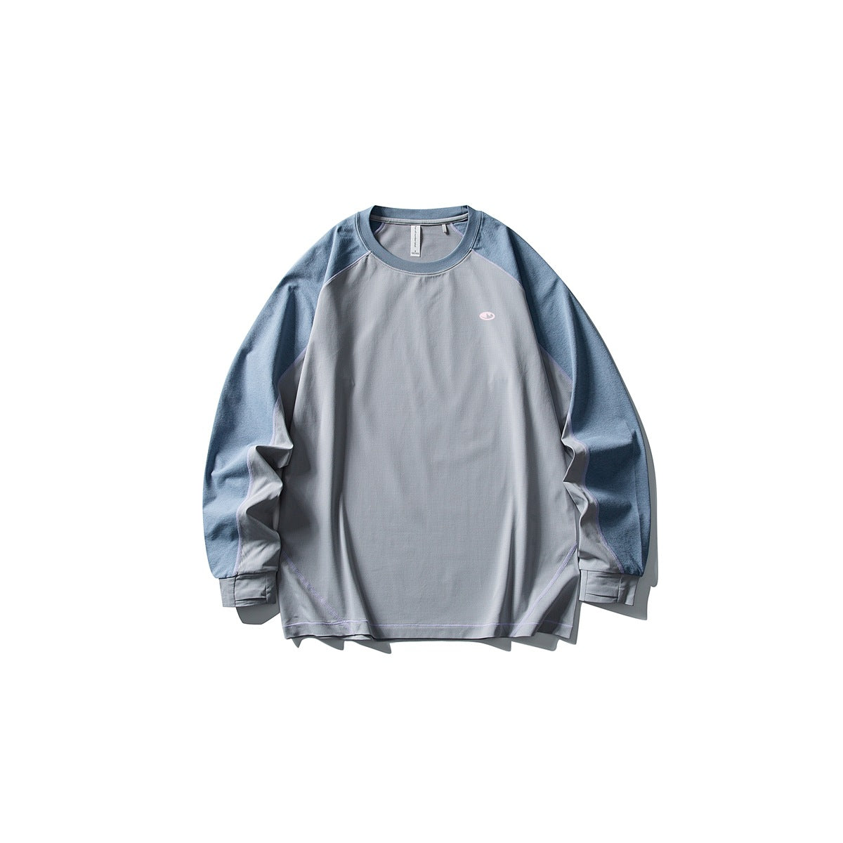 Front of a light gray long-sleeve shirt with blue raglan sleeves, lavender piping, and a small chest emblem.