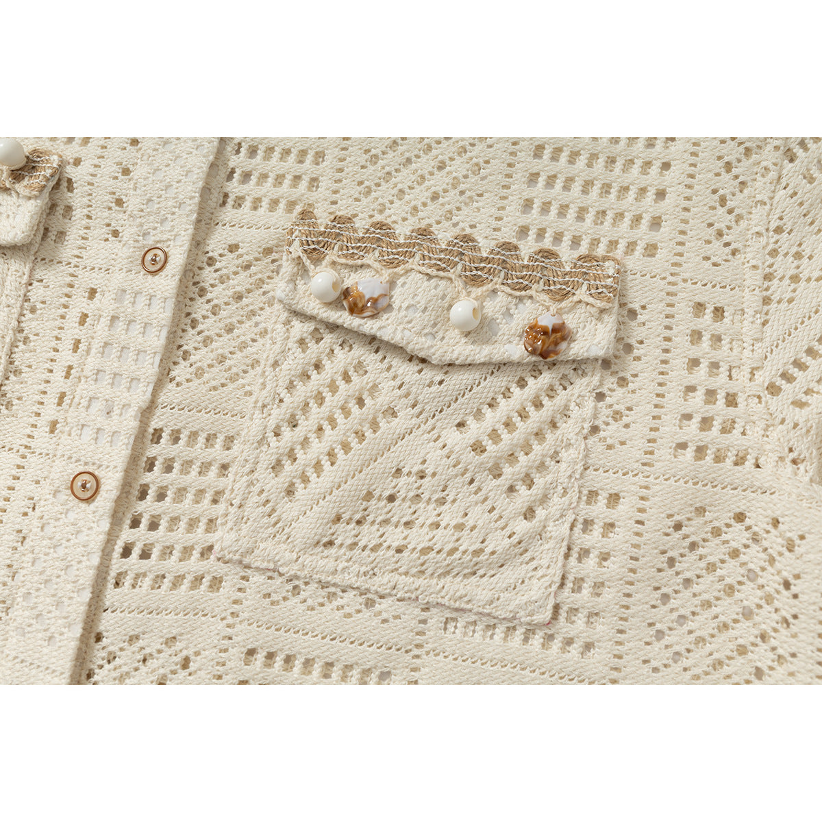Close-up of an ivory openwork shirt’s chest pocket with decorative trim and ornamental buttons.