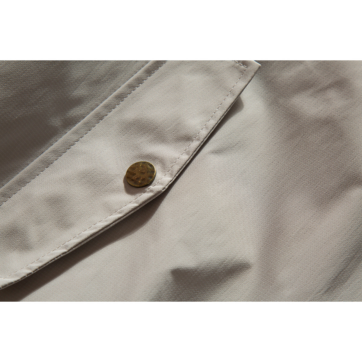 Close-up of a brass-tone button on the stitched front placket of a light beige jacket.