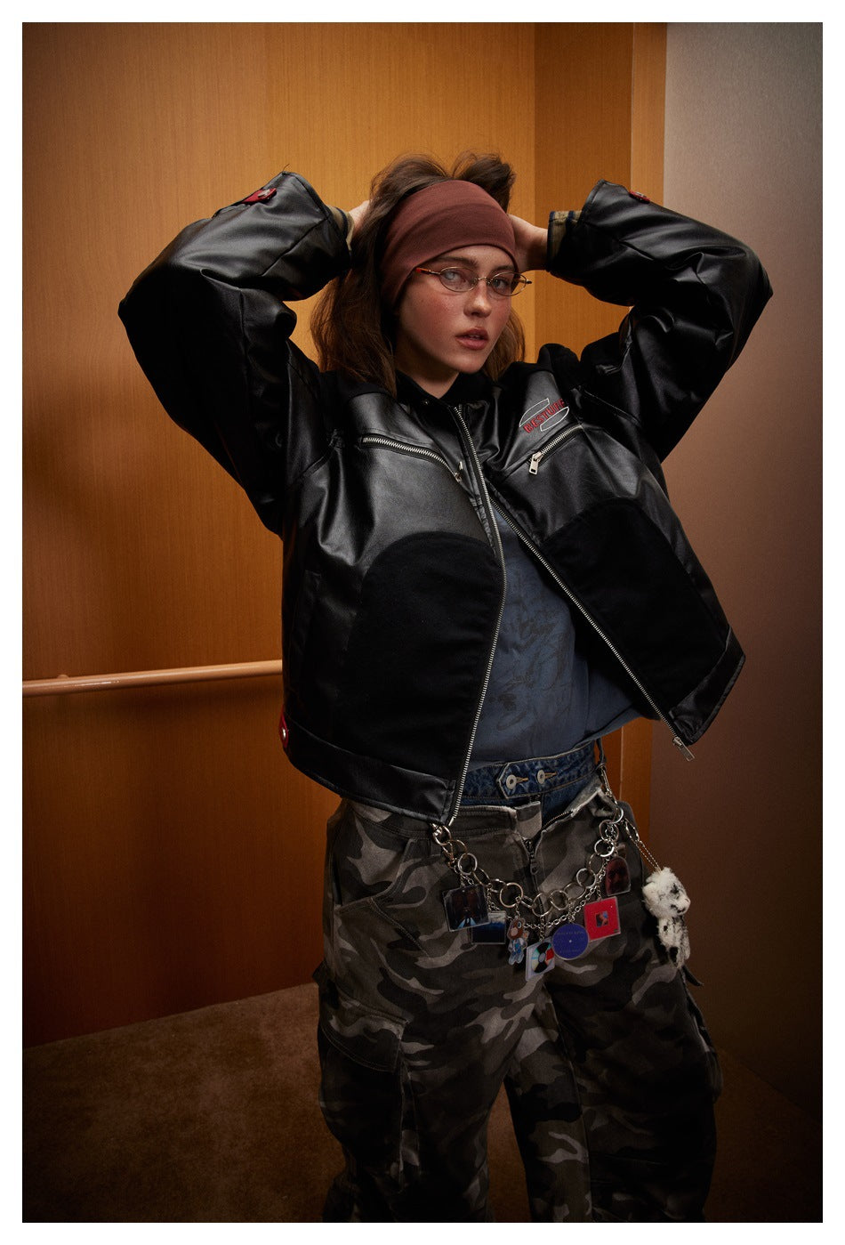 Model wearing a black color-block zip jacket with silver zippers and chest logo, posed with arms raised.