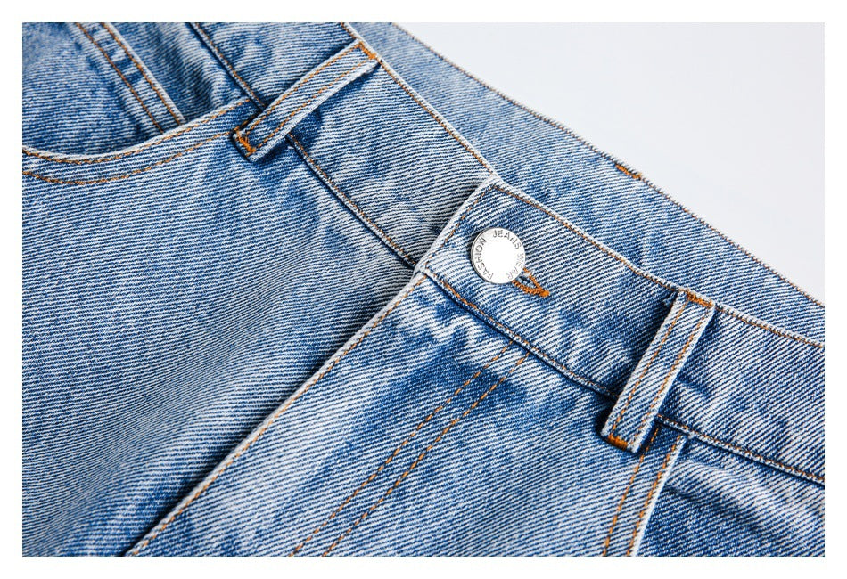 Close-up of the jeans’ metal waist button, belt loop and contrast stitching on light-wash denim.