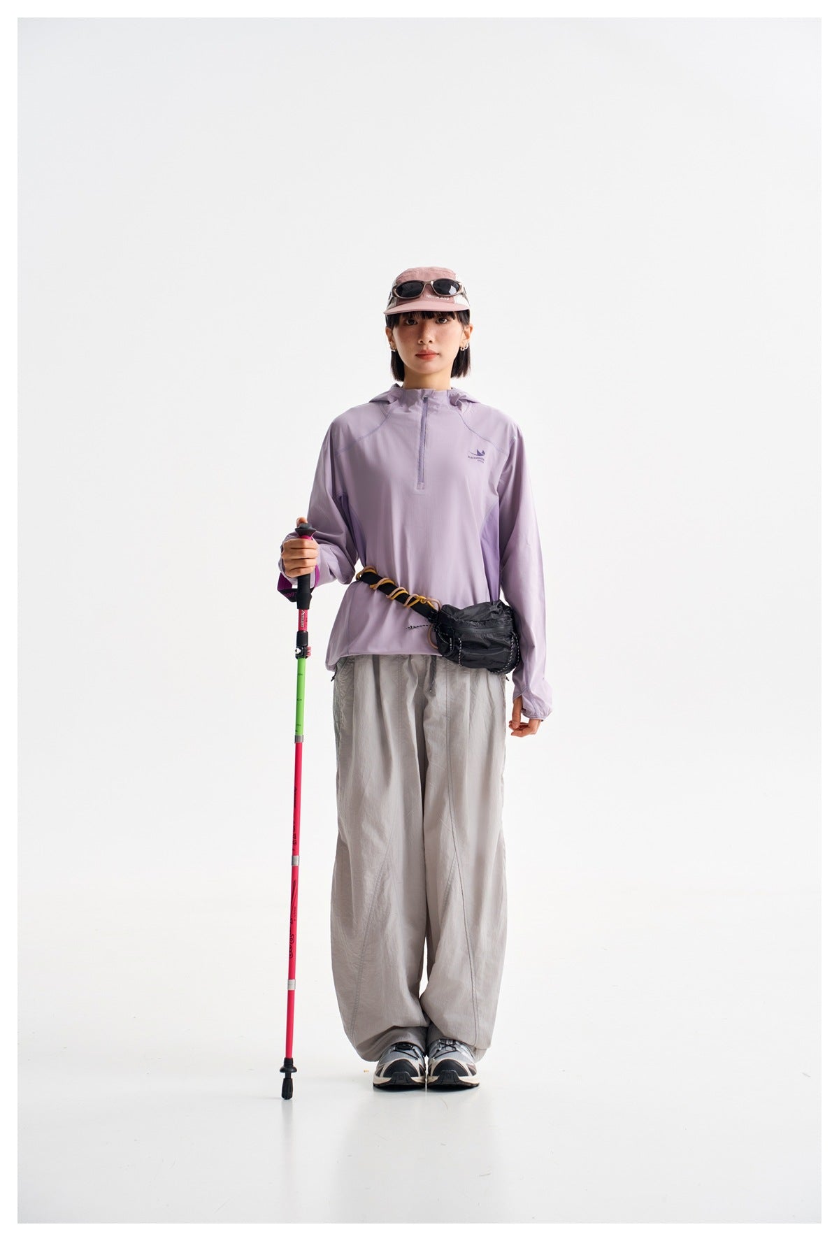 Model wearing a light lavender hooded pullover with a short front zipper and loose light gray pants, facing forward.