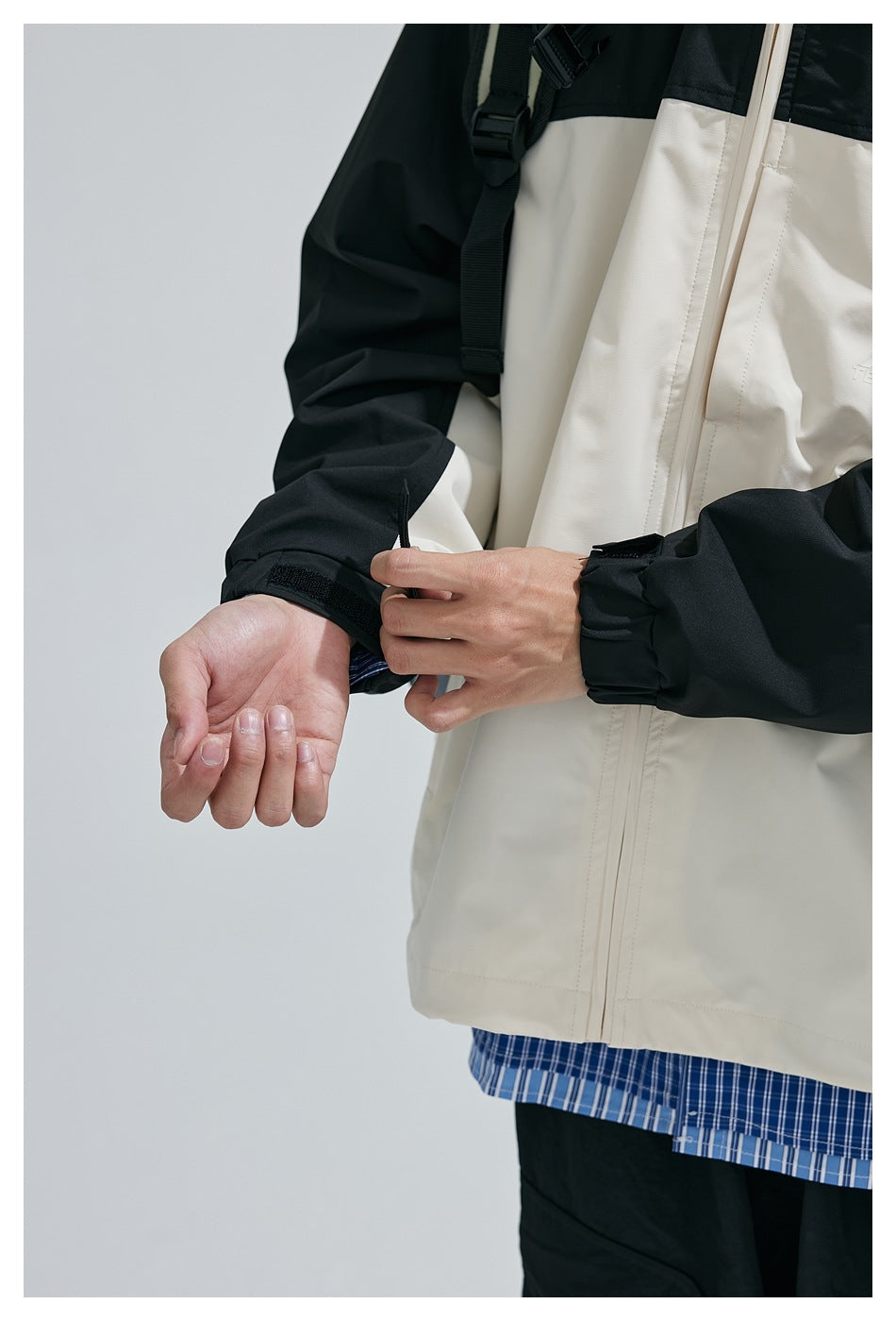 Close-up of the jacket's black sleeve, adjustable cuff tab, cream front panel, and zipper.