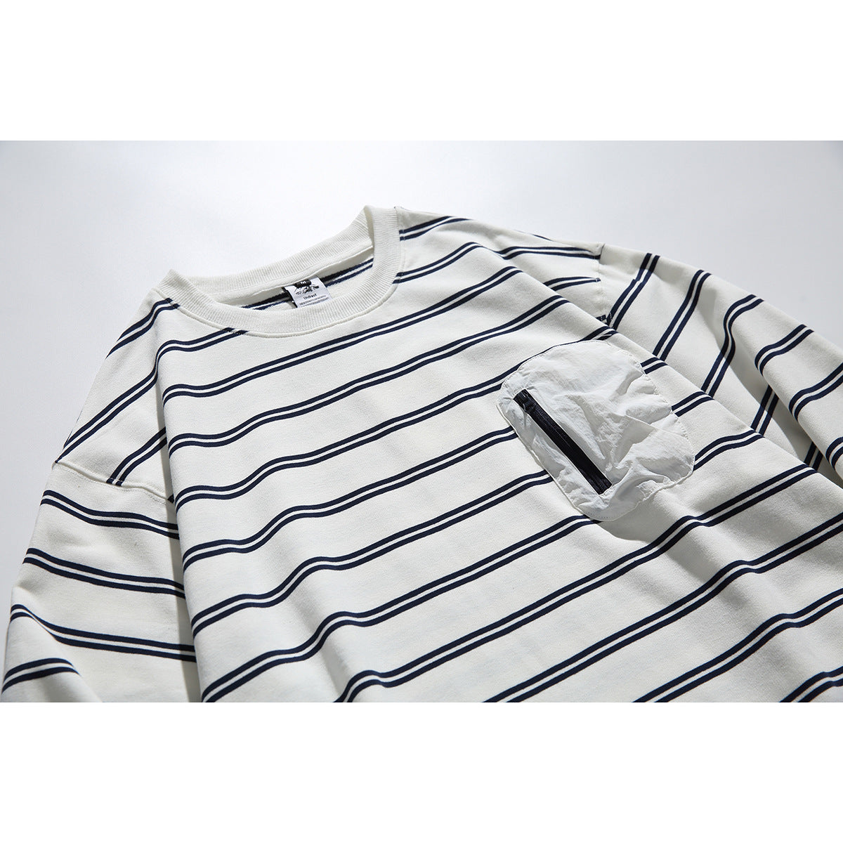 Close-up of an ivory long-sleeve shirt with navy stripes and a crinkled chest pocket with a black zipper.