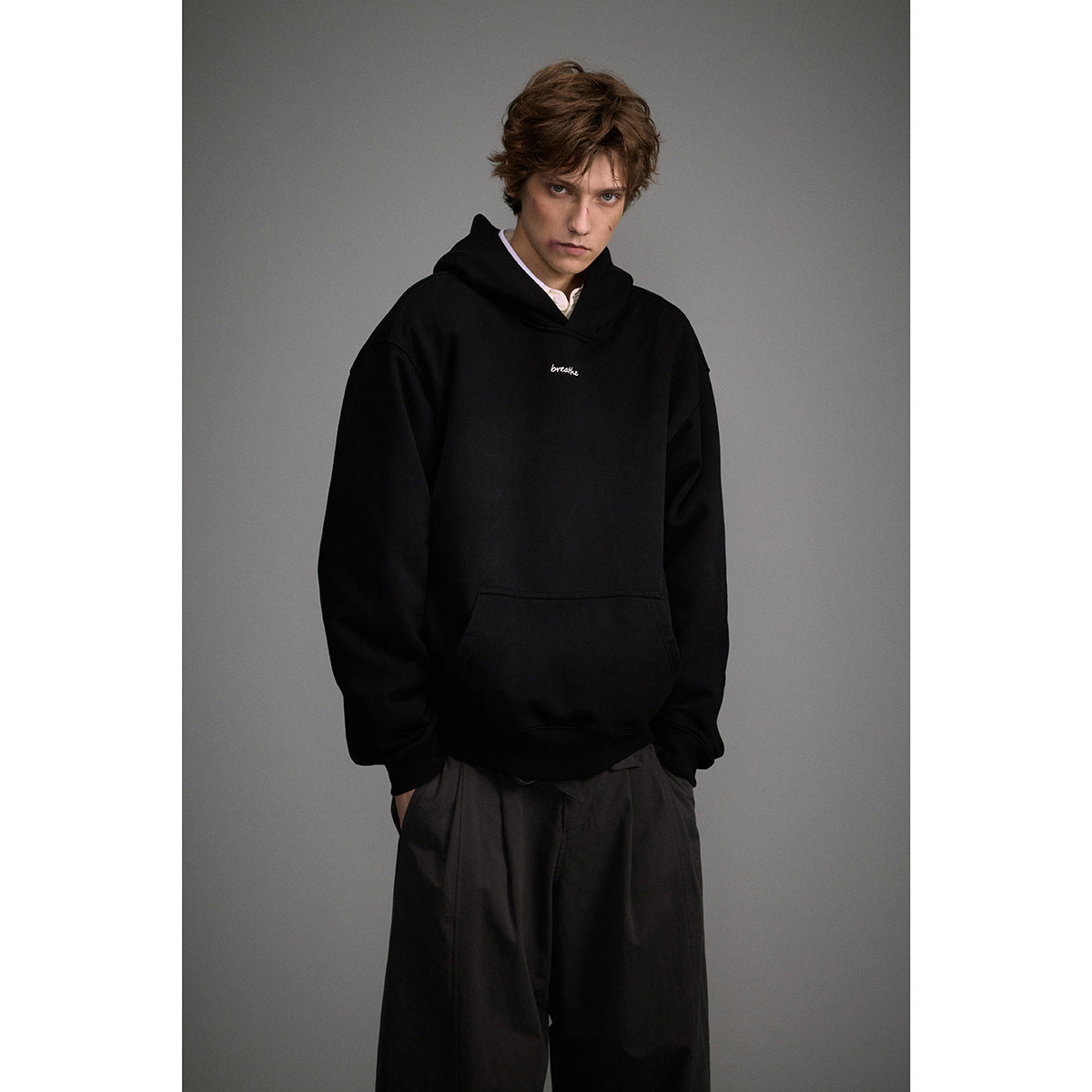 Model wearing a black oversized hoodie with a kangaroo pocket and small white chest script.