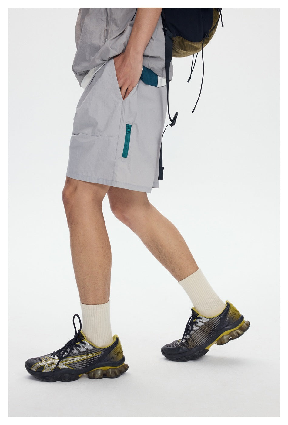 Side view of model wearing light gray shorts showing teal side zipper detail, cream socks and sneakers