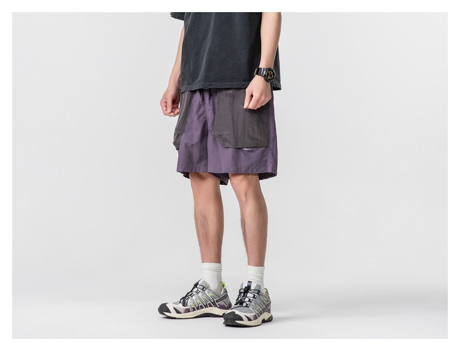 Cropped model wearing muted purple shorts with oversized gray patch pockets, front three-quarter view.