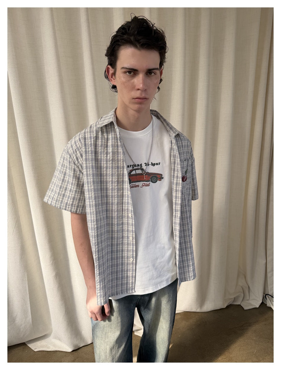 Close front view highlighting a blue-gray plaid short-sleeve shirt worn open over a white car-graphic tee.