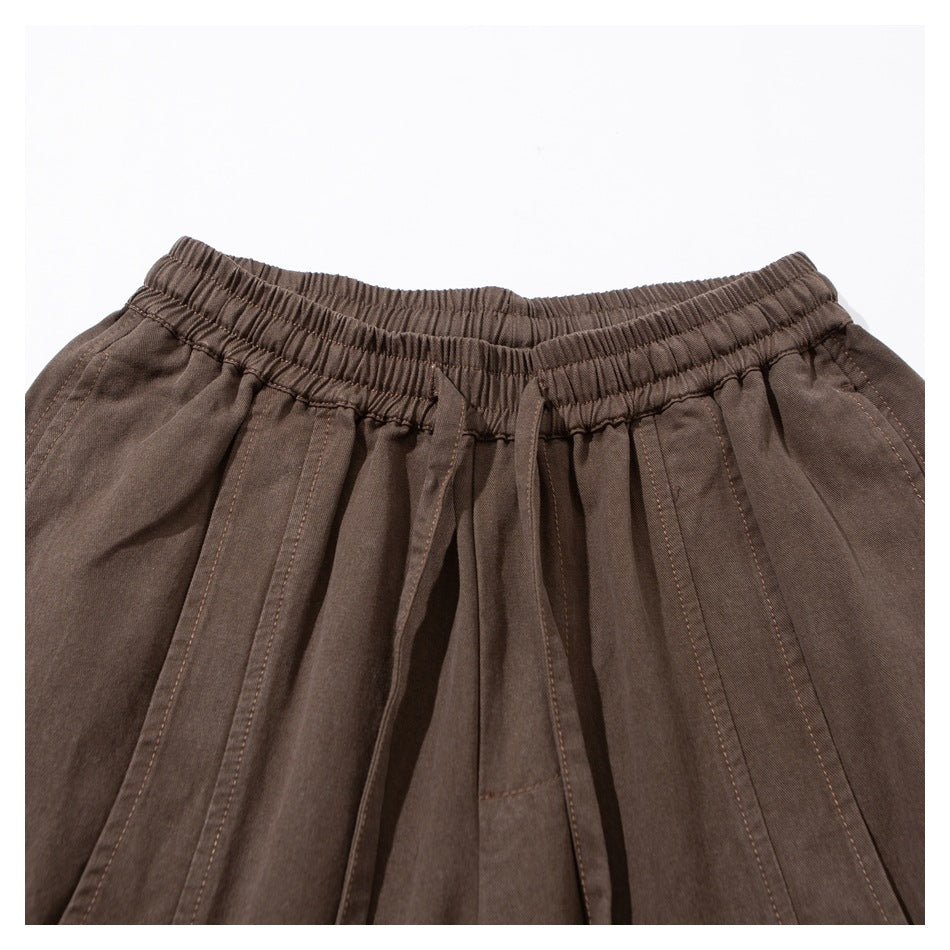 Close-up of brown pants showing the gathered elastic waistband, drawstring, and stitched pleats.