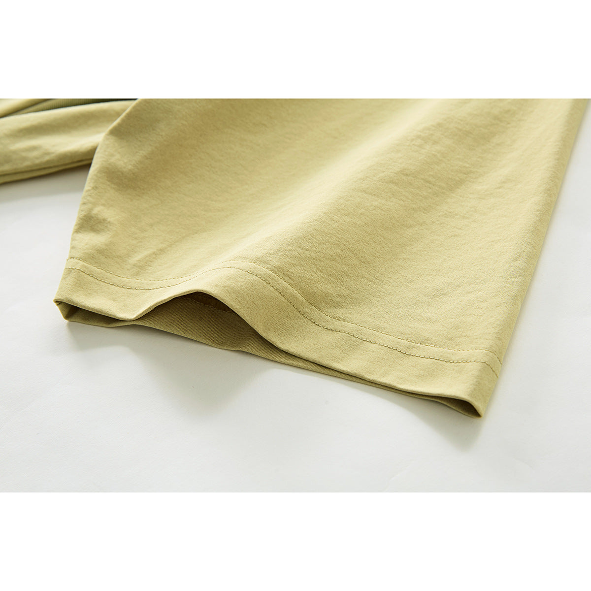 Close-up of the pale yellow-green T-shirt's short sleeve hem and stitching on a white background.
