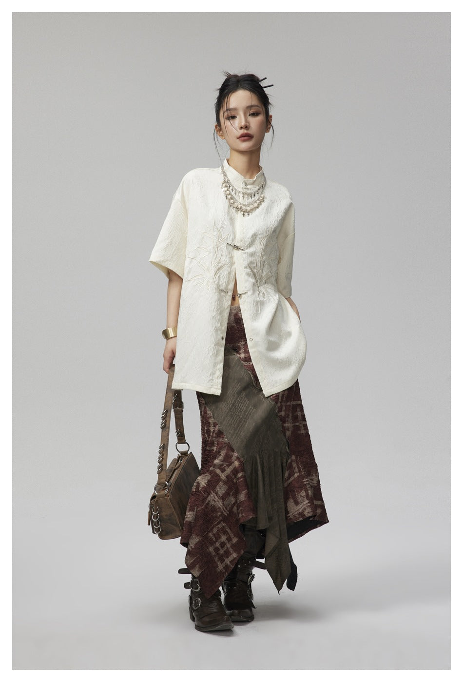 Model wearing the beige embroidered short-sleeve stand-collar shirt open at the front over a long patterned skirt