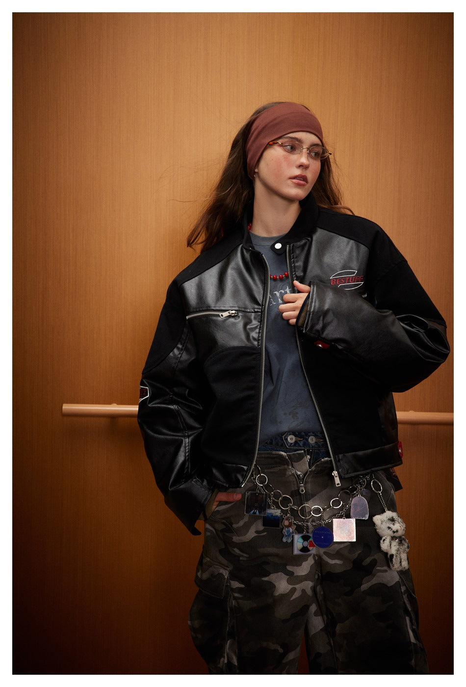 Model wearing a black jacket with glossy panels and zip pockets, paired with camouflage trousers.