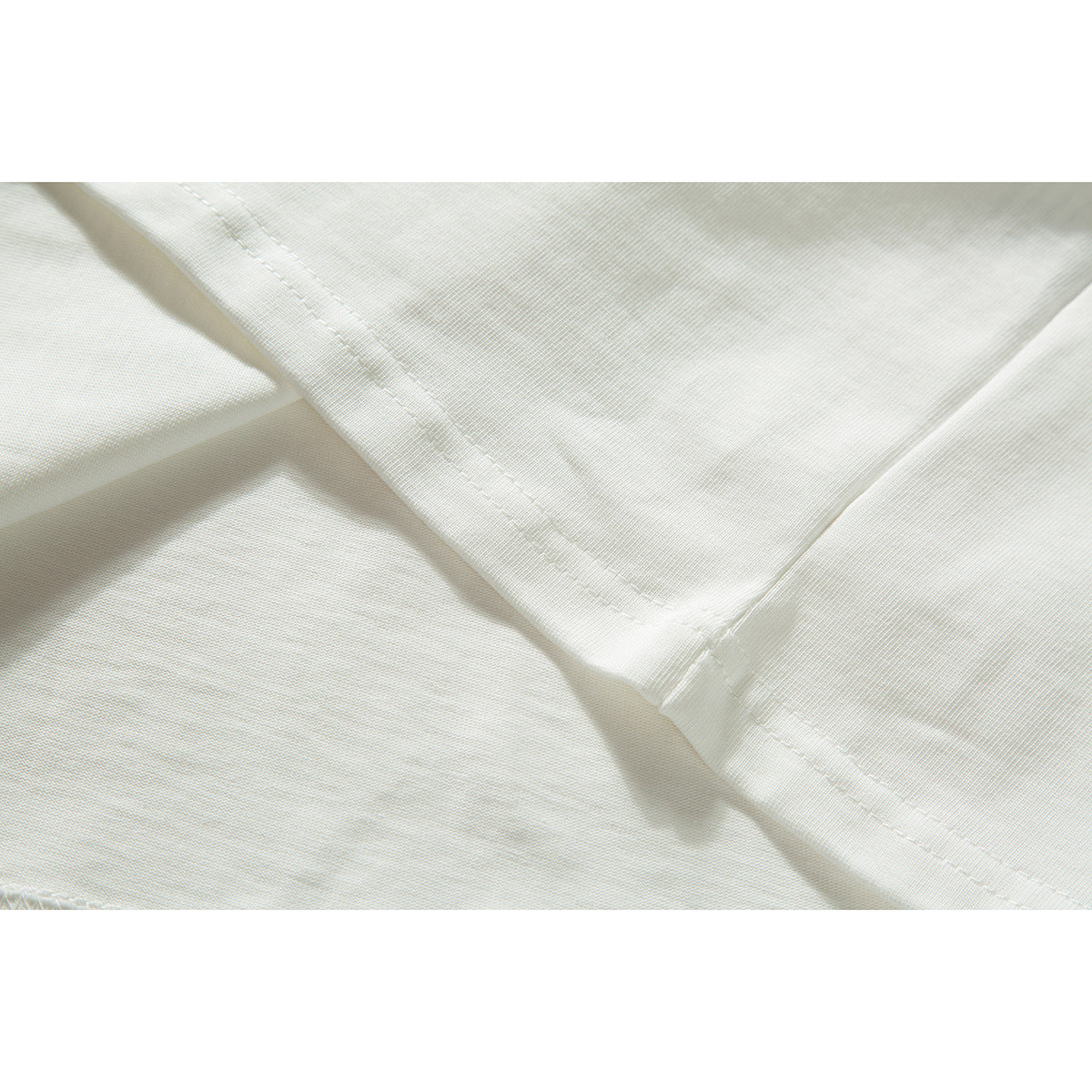 Close-up of ivory T-shirt fabric and intersecting stitched seams.