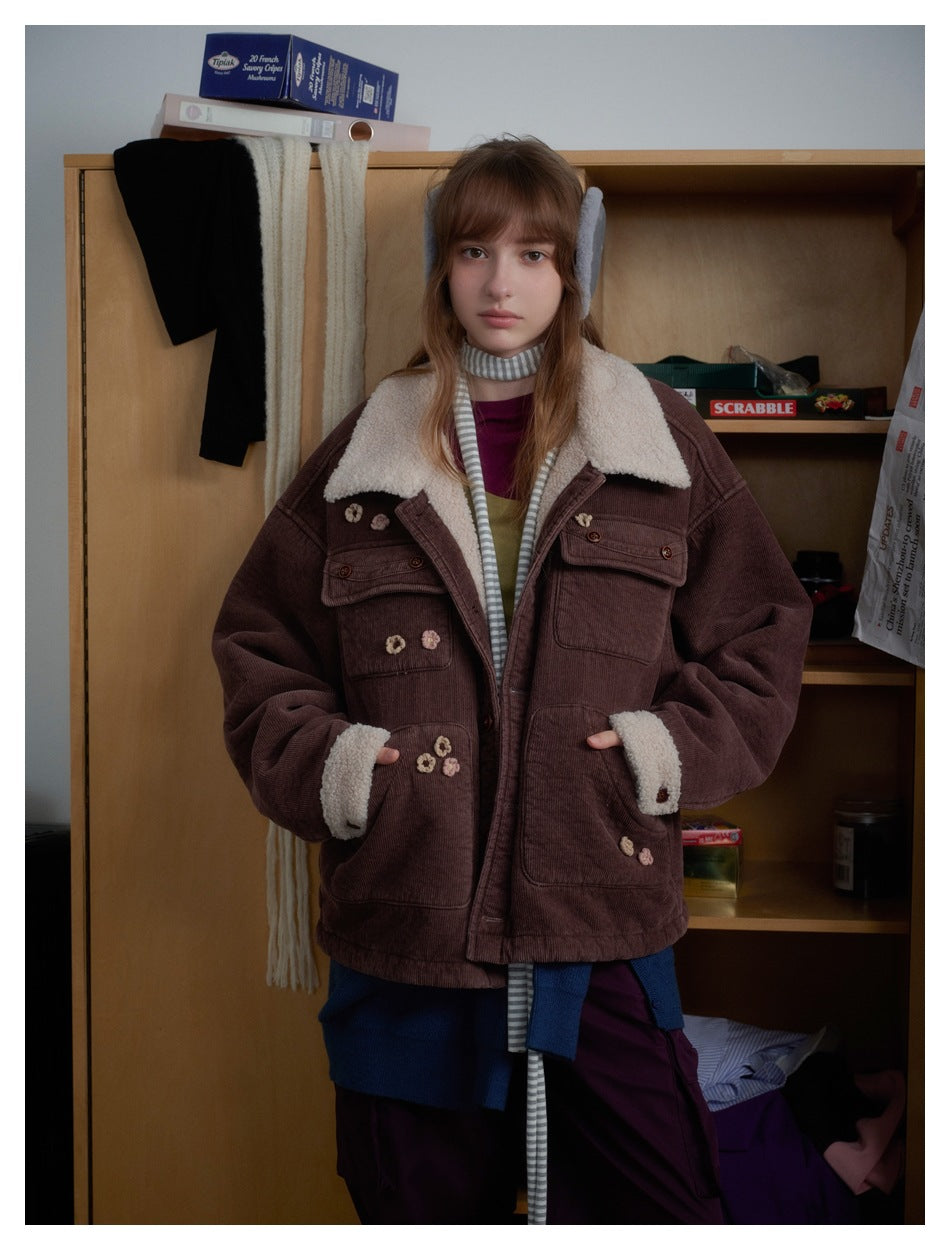 Front view of a model wearing a brown corduroy jacket with a cream shearling collar and cuffs, floral appliqués, and patch