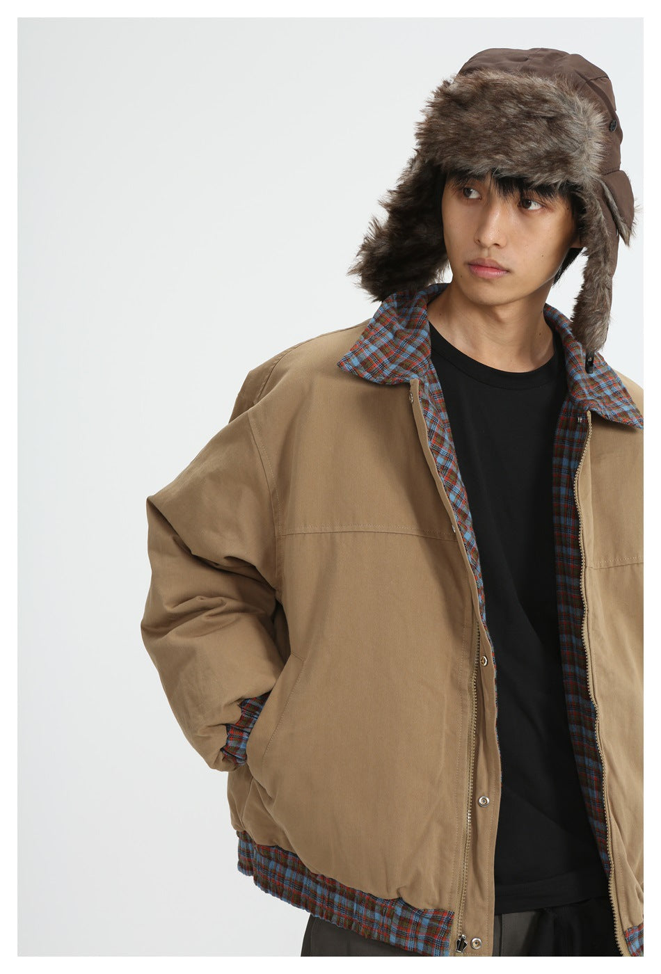 Person wearing a tan jacket with blue plaid lining and a brown fur-trimmed trapper hat.