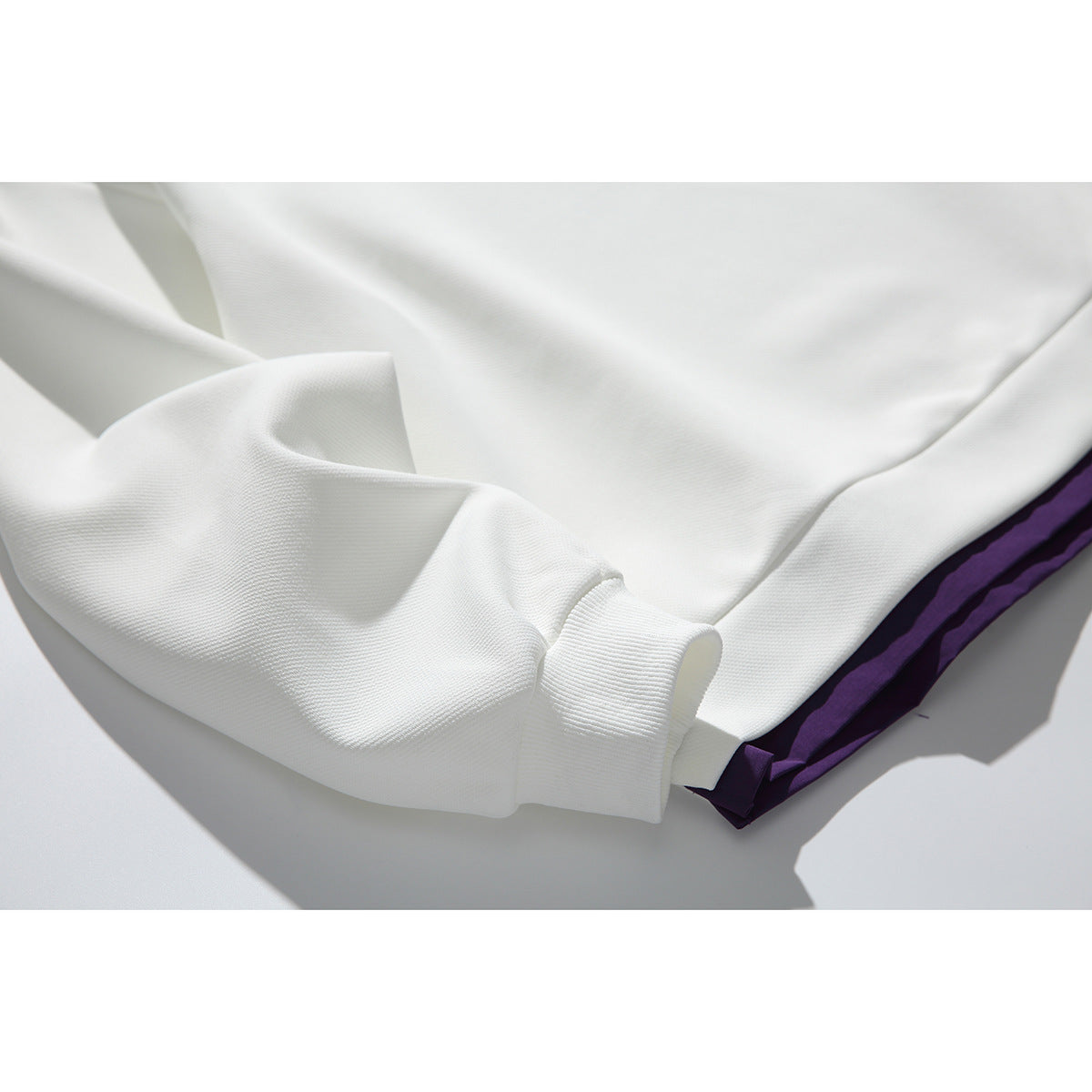Close-up of the ivory sweatshirt’s ribbed cuff and hem, with a purple layer visible underneath.