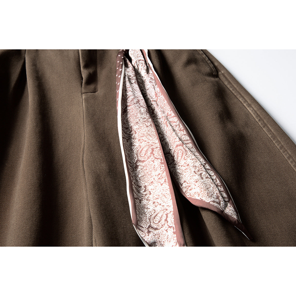 Close-up of brown trousers with a pink-and-cream paisley scarf tied at the waistband.