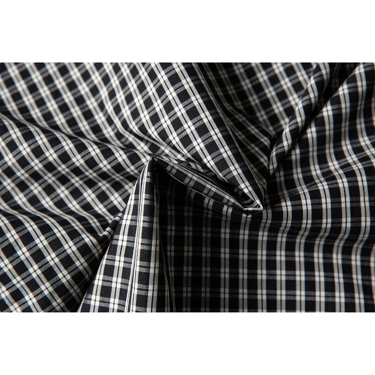 Close-up of black fabric with a white and gray plaid pattern, folded to show its surface.