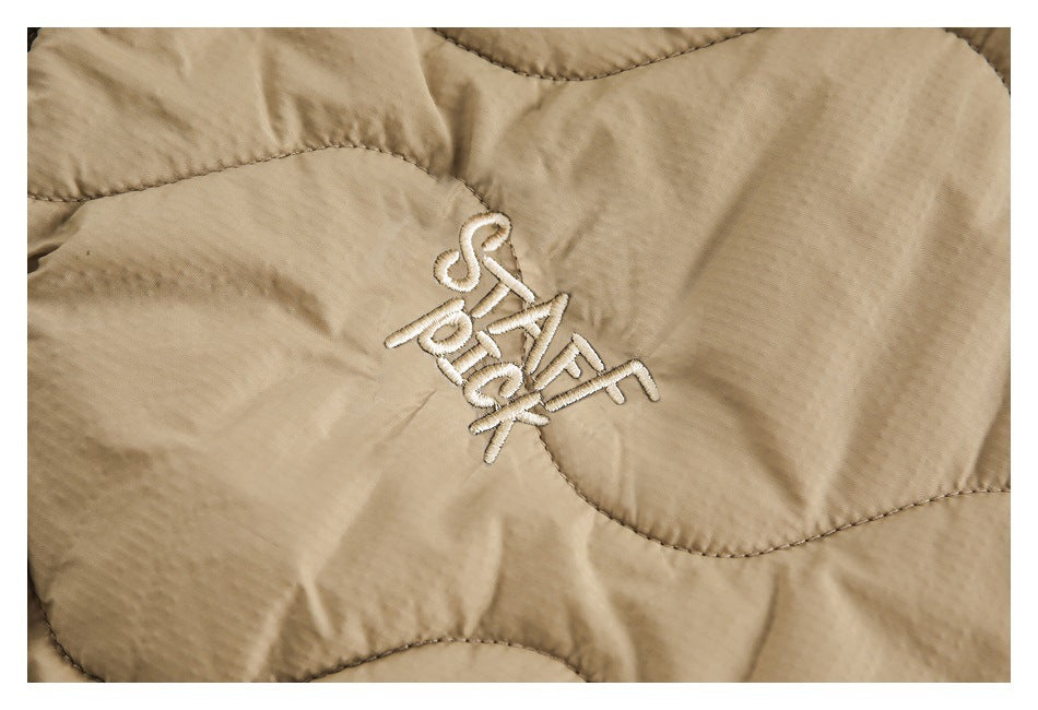 Close-up of white embroidered lettering on a beige quilted jacket.