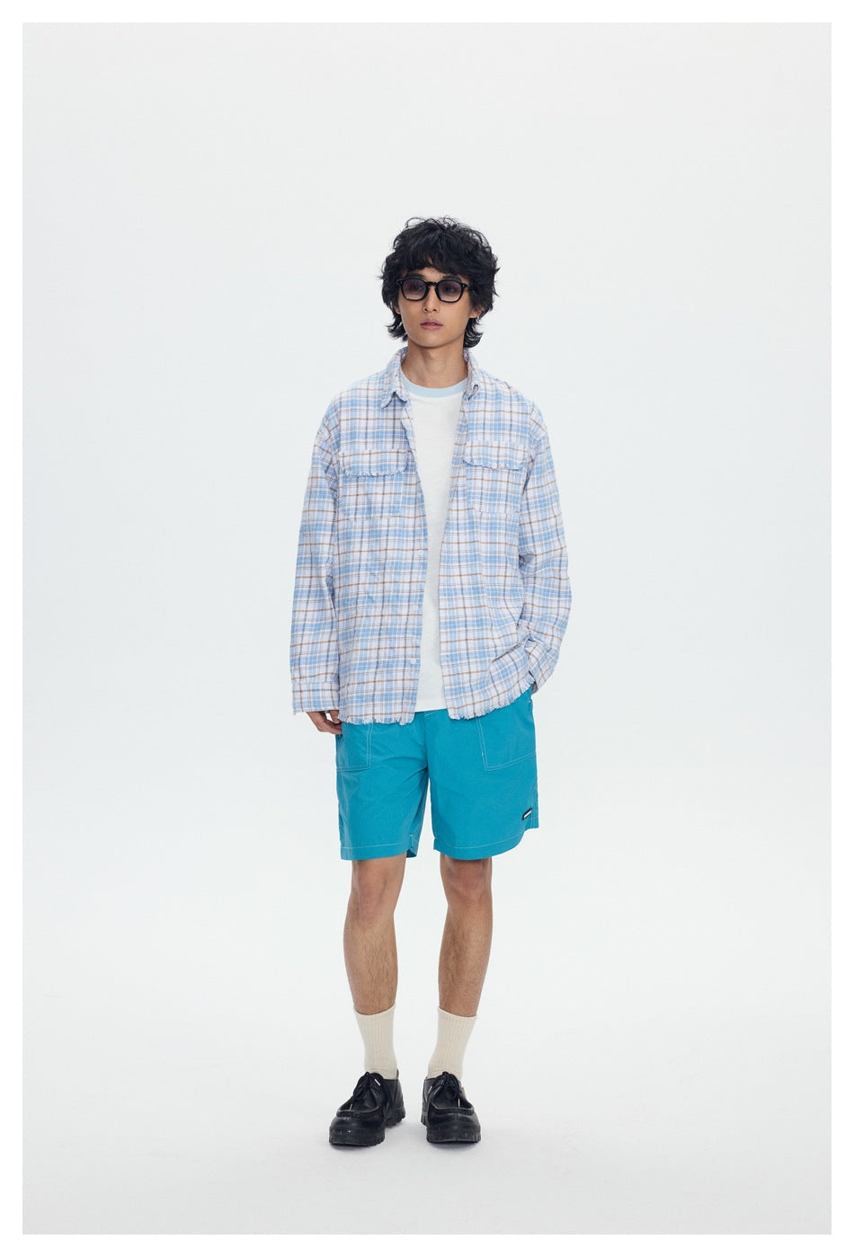 Front view of a model wearing an open blue-and-tan plaid shirt over a white T-shirt with turquoise shorts.