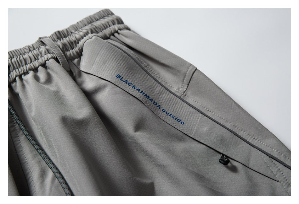 Close-up of gray pants with an elastic waistband, zip pocket, and BLACKARMADA outside text on the garment.