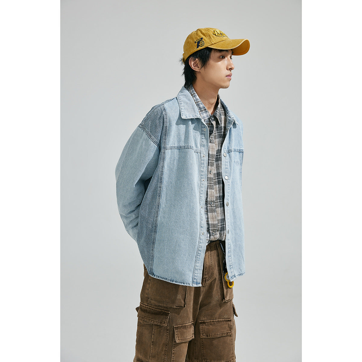 Model wearing an oversized light-blue denim jacket with darker contrast panels, a plaid shirt, brown cargo pants and a yellow