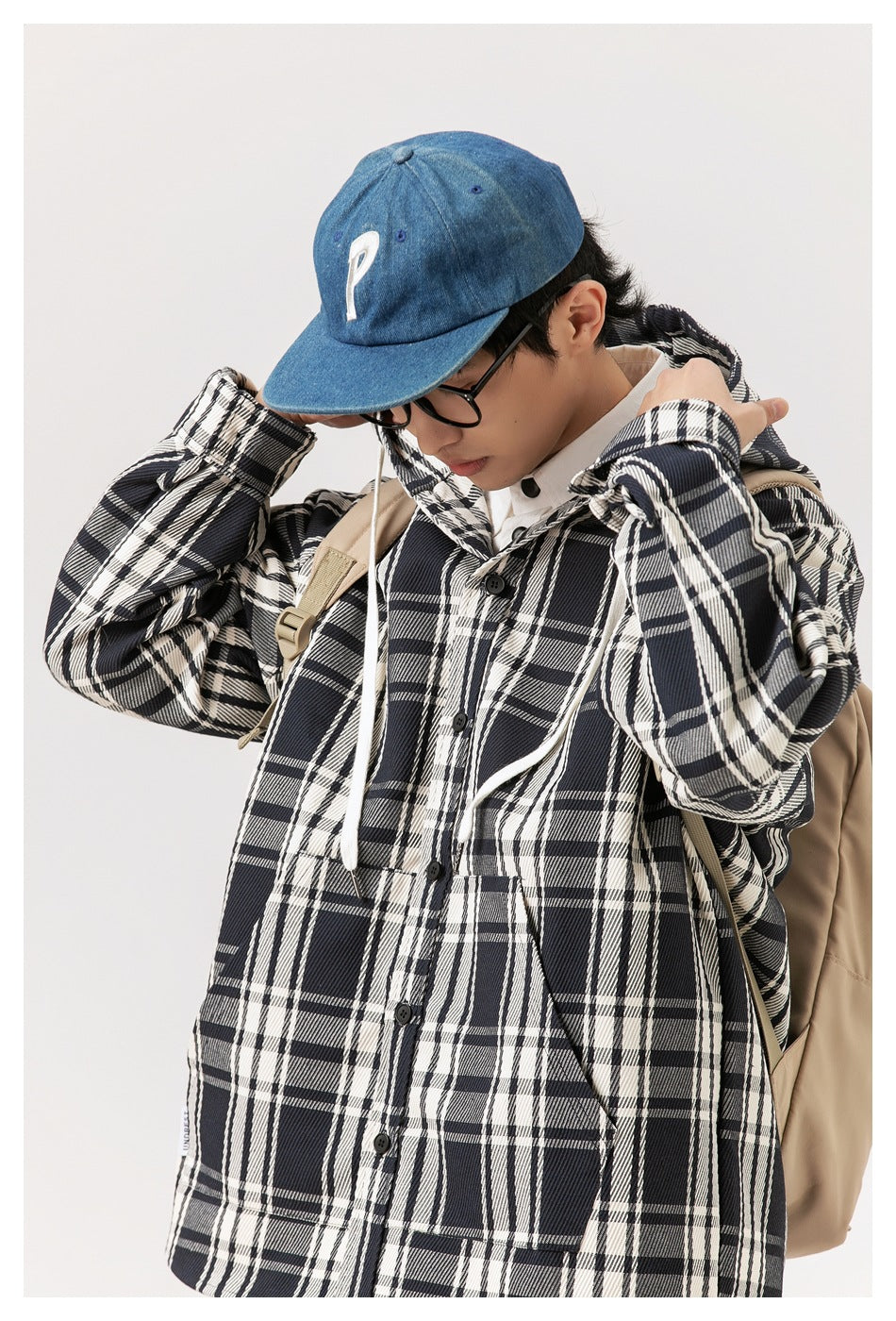 Angled view of a model wearing a black-and-white plaid hooded coat with white drawstrings and front buttons.