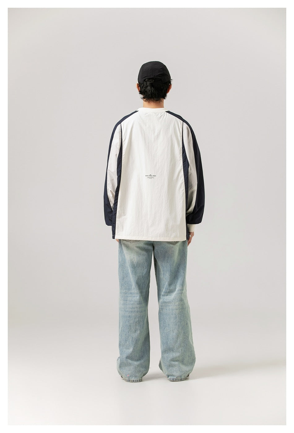 Full-length rear view of a model wearing an ivory and navy color-block pullover with light-wash wide-leg jeans.