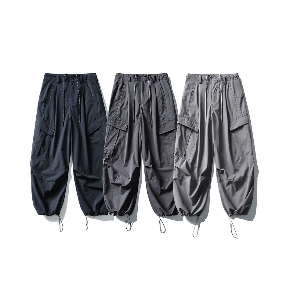 Three front views of wide-leg cargo pants in black, charcoal, and light gray, with drawstrings and gathered hems.
