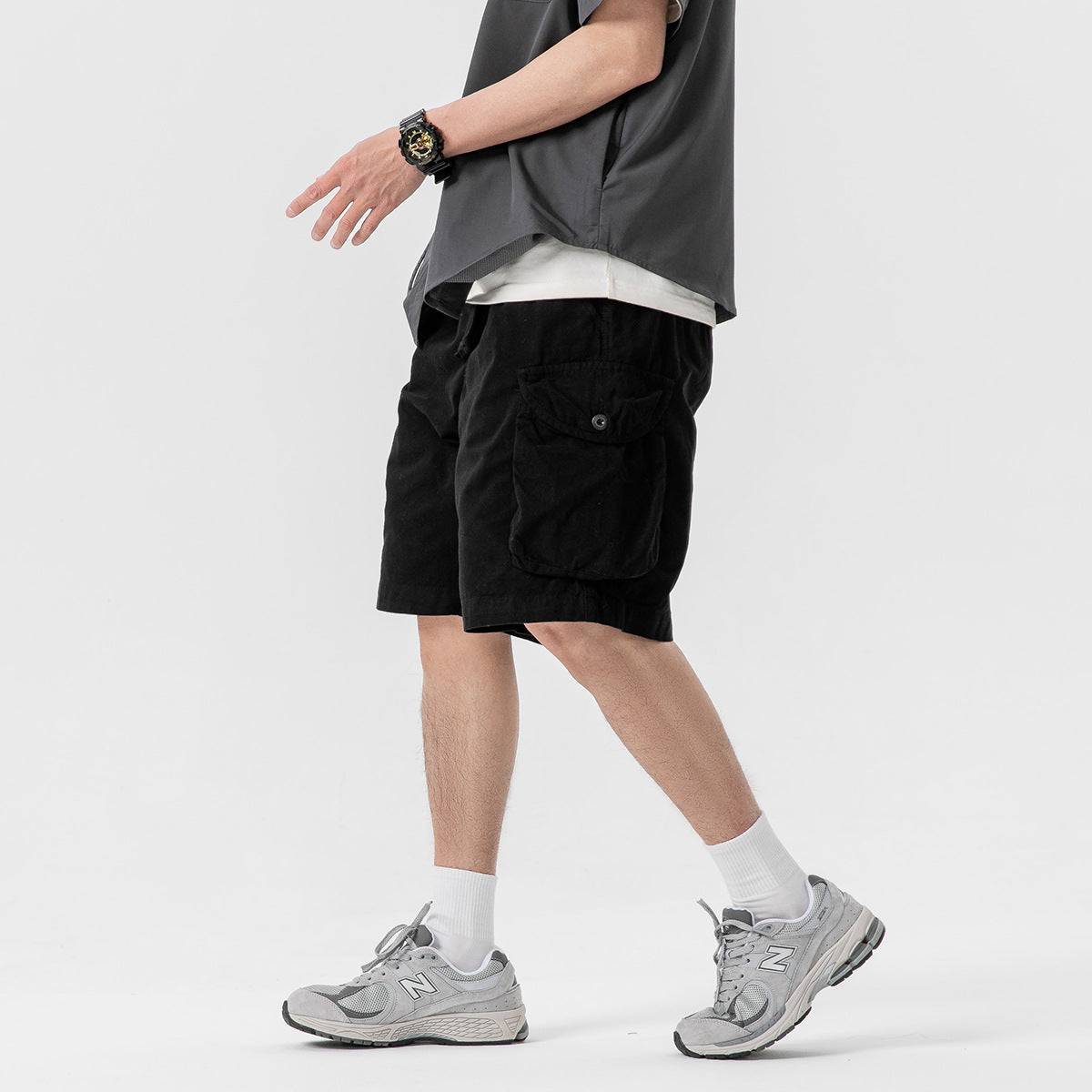 Side view of a model wearing black cargo shorts with a buttoned flap pocket.