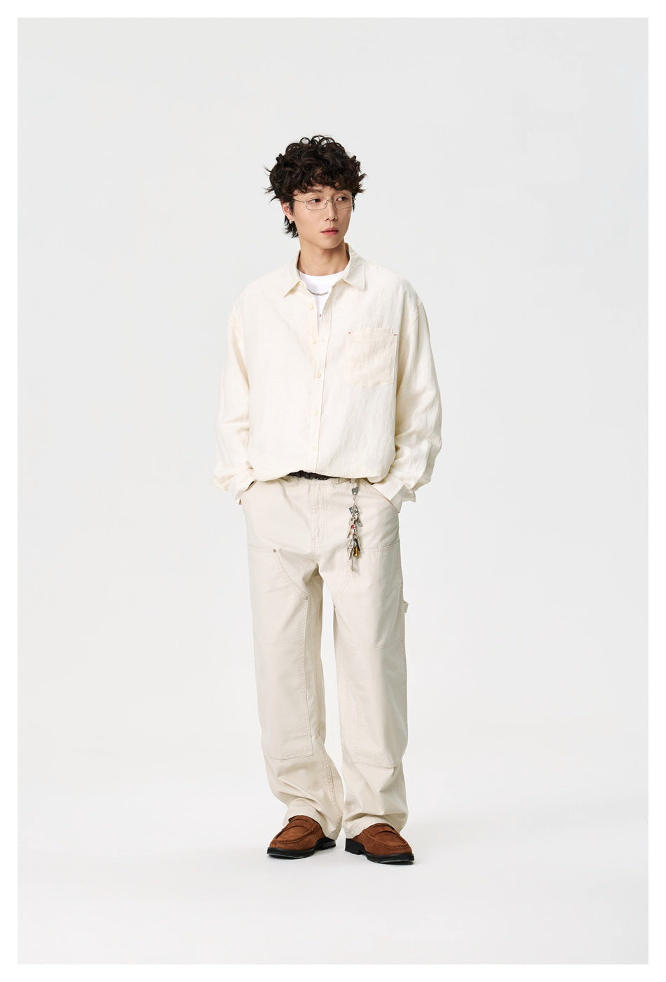 Full-length view of a model in an ivory button-up shirt, matching relaxed trousers, and brown loafers.