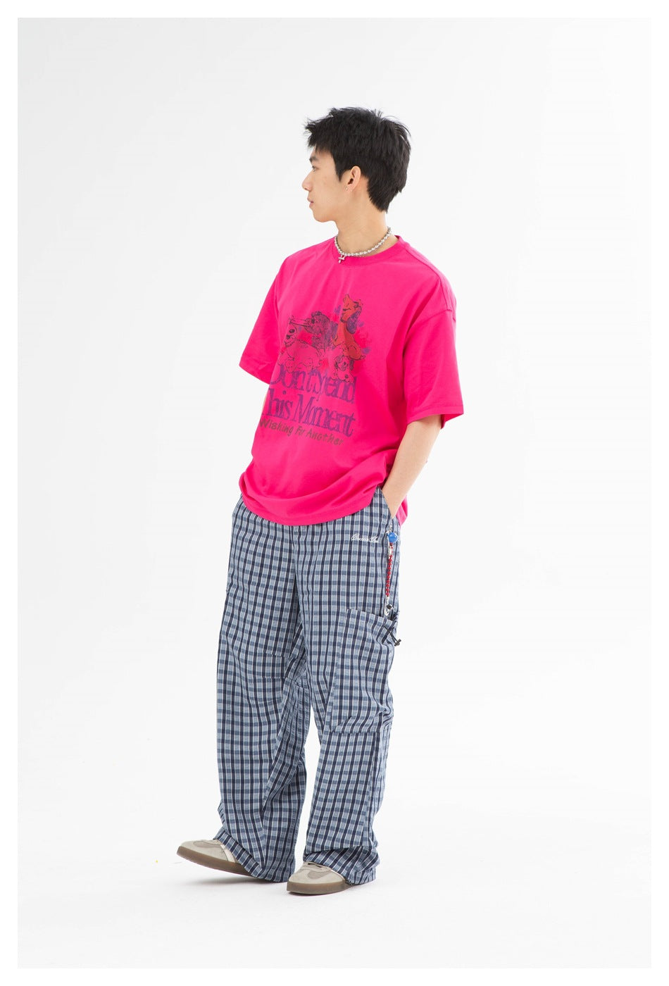 Full-length side view of a model in a hot-pink graphic T-shirt and loose blue plaid trousers.