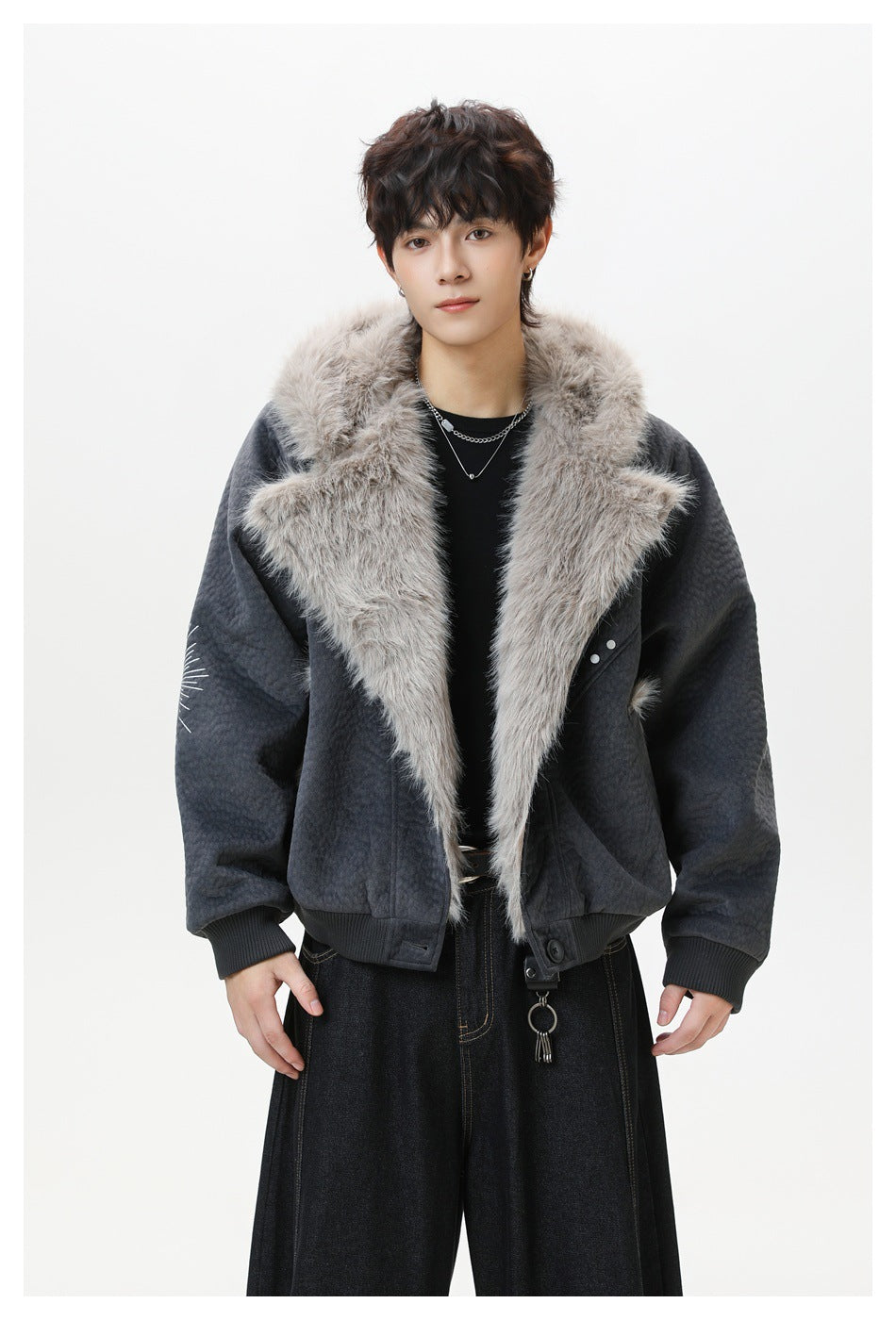 Model wearing dark gray textured jacket open with wide fluffy fur-like lapels, black top and dark wide-leg jeans
