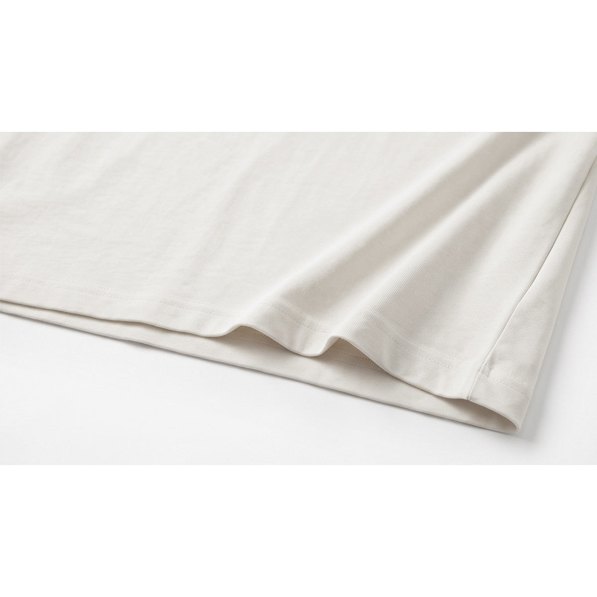Close-up of the plain white shirt hem and side seam laid flat.