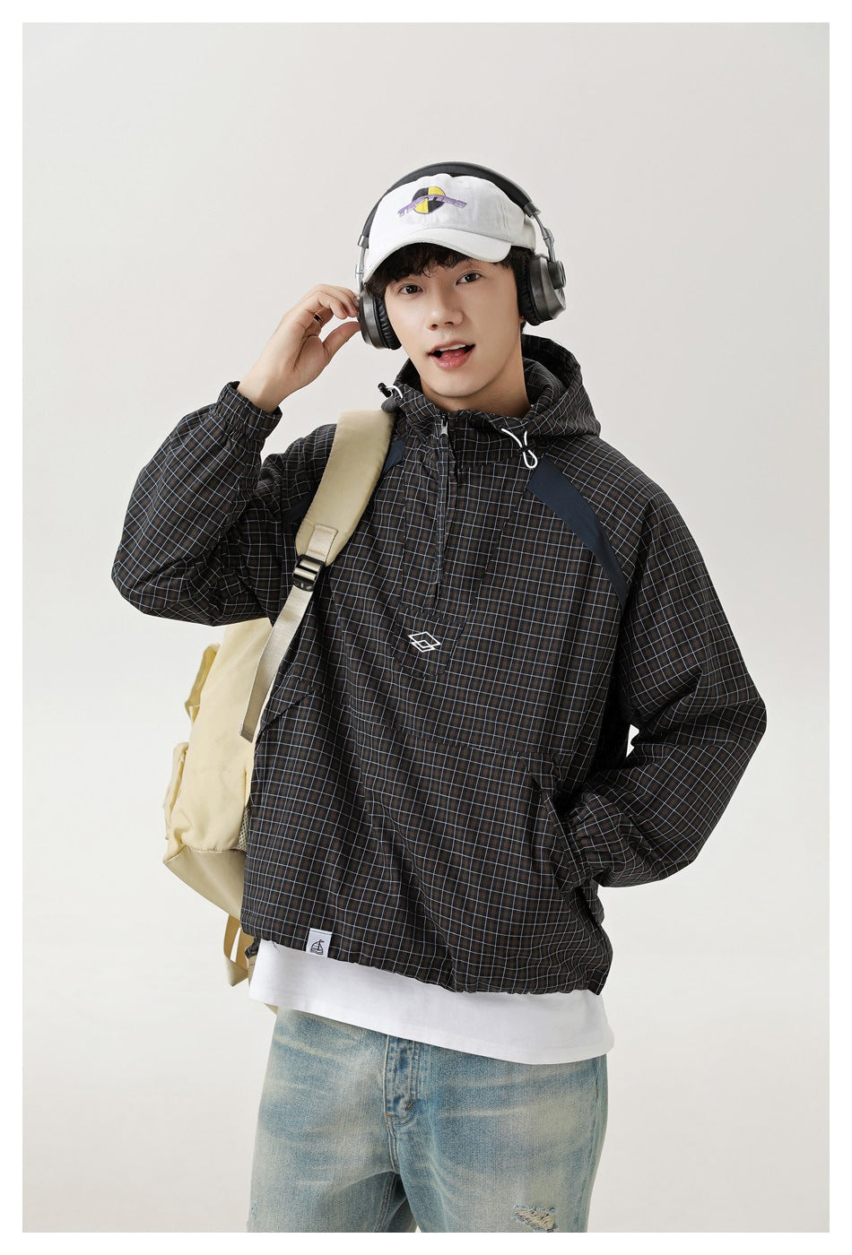 Model wearing a dark grid-plaid hooded pullover jacket with contrast shoulder panels and a front pouch pocket.