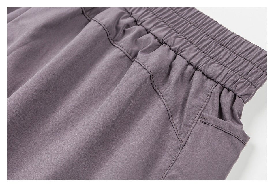 Close-up of mauve-gray shorts showing the elastic waistband and stitched side pocket opening.