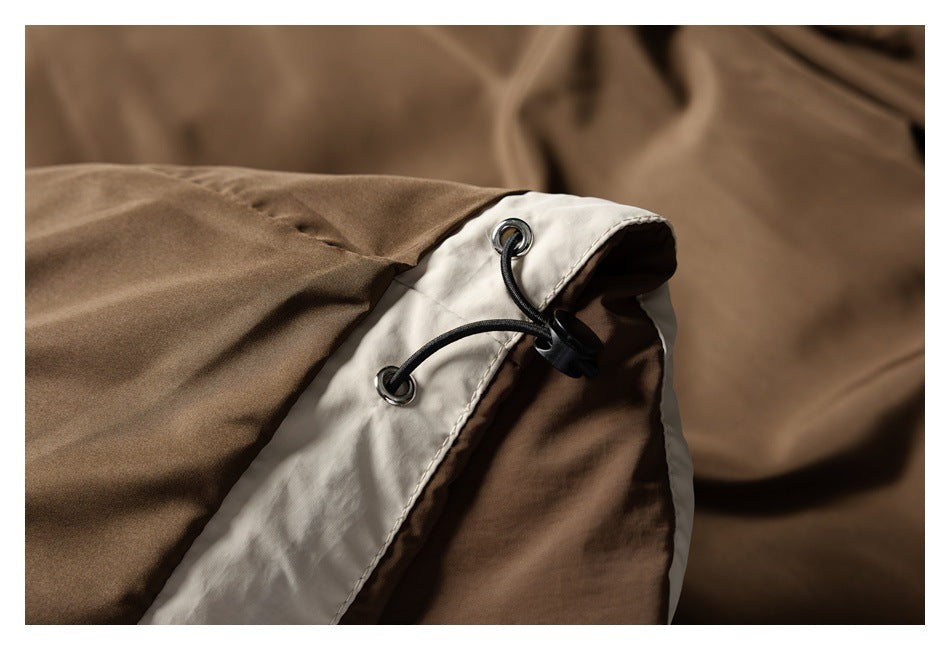 Close-up of a brown garment edge with cream trim, metal eyelets, and a black adjustable drawcord.