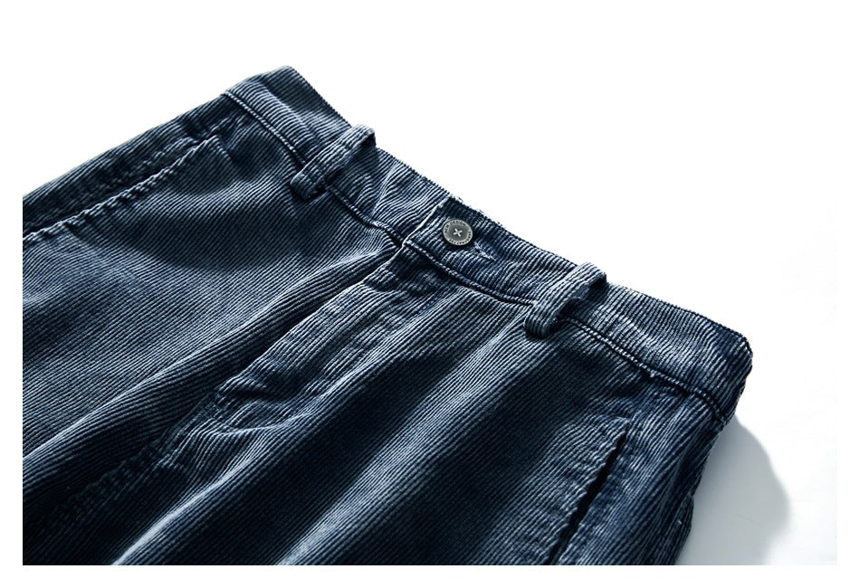 Close-up of dark blue corduroy trousers showing the front waistband, button, belt loops and pocket.