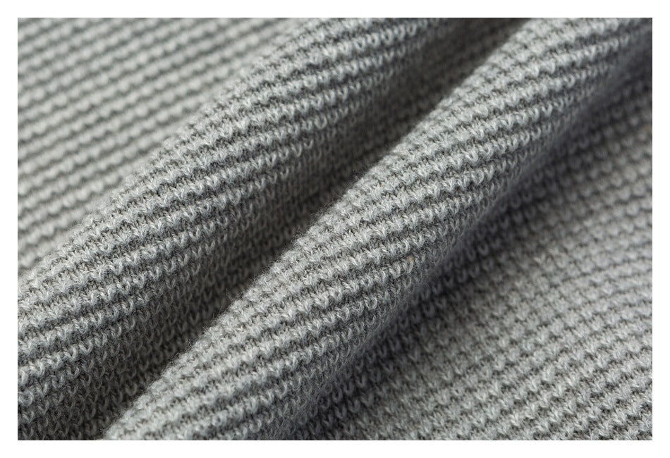 Macro view of the light gray sweater’s raised knit texture and folded fabric.