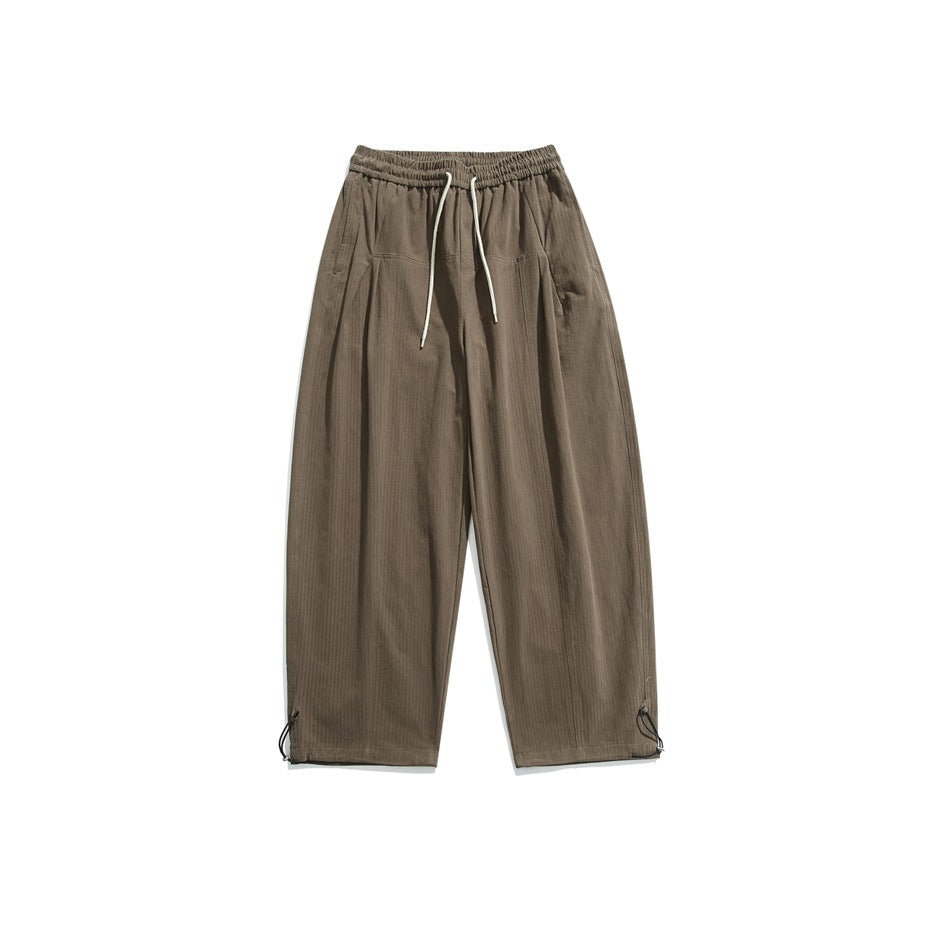 Brown wide-leg drawstring pants with elastic waistband, front pleats and toggle hem cinches, flat lay on white